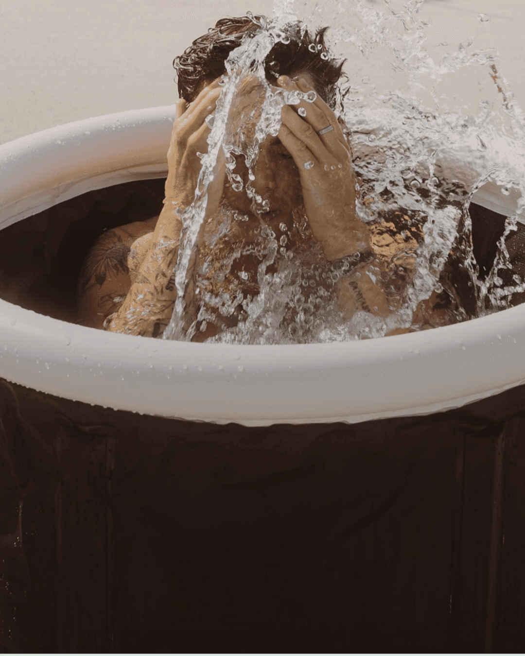 man sitting in an ice bath splashing his face